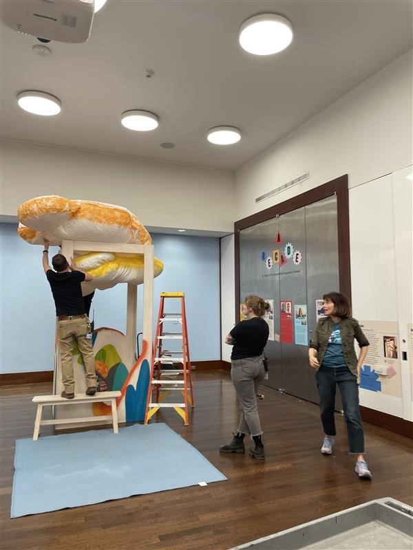 Museum staff installing cloud-like forms in a gallery.