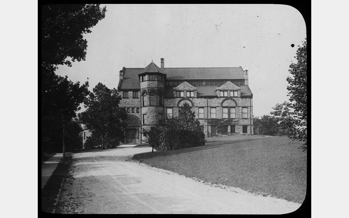 Black and white photo of a road leading to a stone building with a tile roof.