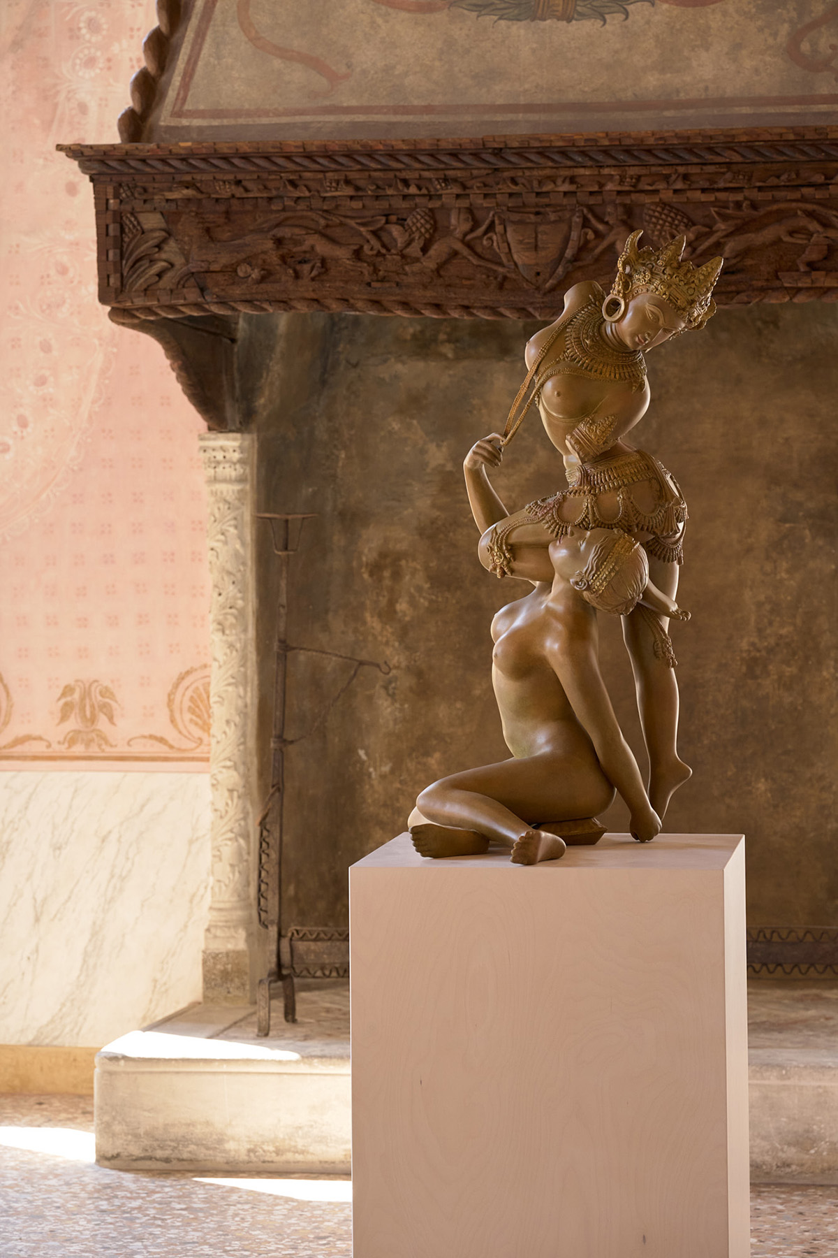 A sculpture of an ornately dressed nude woman with a knee resting on the shoulder of another, sitting nude woman