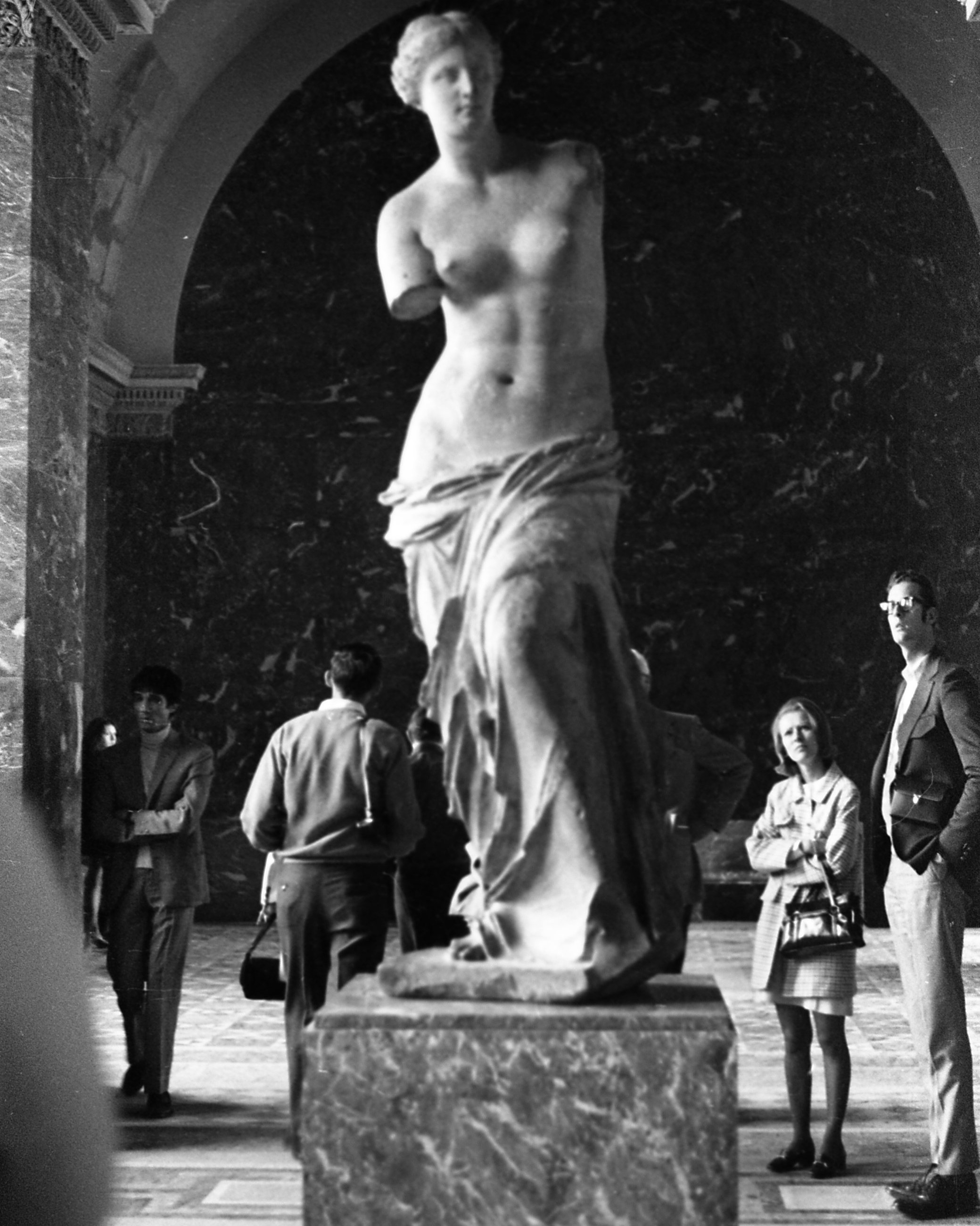 A white marble statue representing a woman; both arms are missing; lower half is covered by drapery; upper half is nude; hair is pulled back.