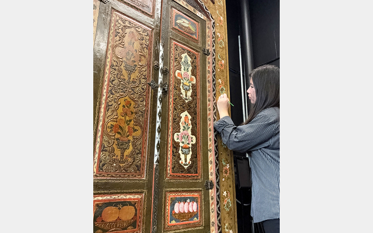 Woman using a brush to remove varnish from a decorative painted wall panel
