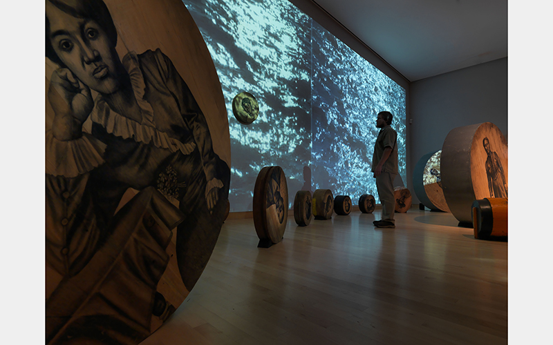 Whitfield Lovell (American, b. Bronx, NY), Deep River, 2013, Fifty-six wooden discs, found objects, soil, video projections, sound, Dimensions variable, Courtesy of American Federation of Arts, the artist, and DC Moore Gallery, New York