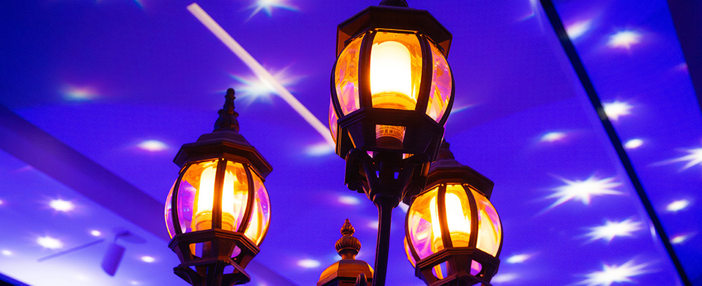 A warm, glowing historic street lamp under a blue, starry ceiling