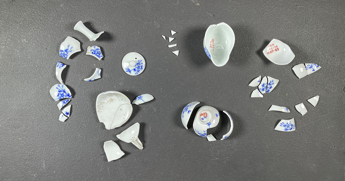 Fragments of a white tea set with blue decorations lay on a table