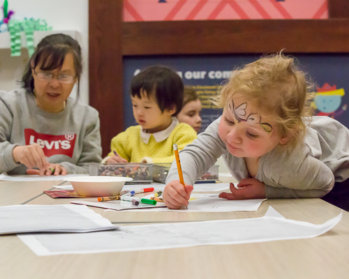 A young child reaches over a table to draw in the REC