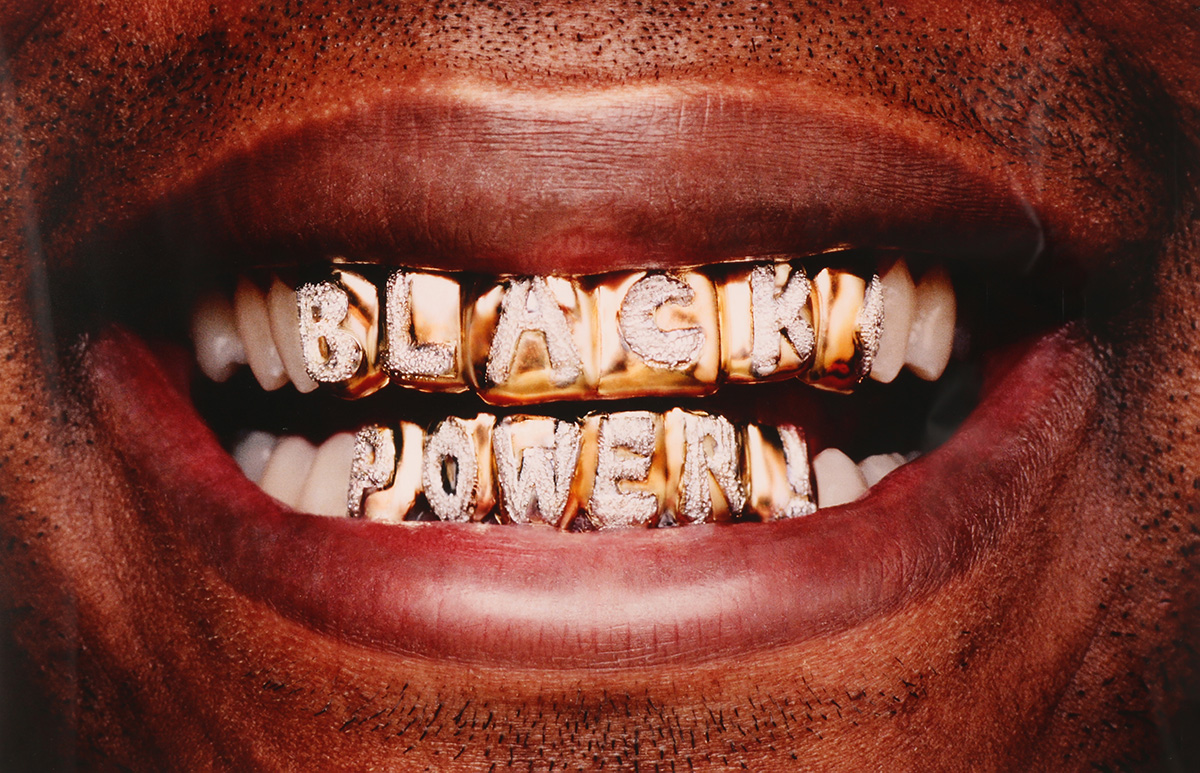 A photo of a Black person's teeth, wearing a grill that says "BLACK POWER"