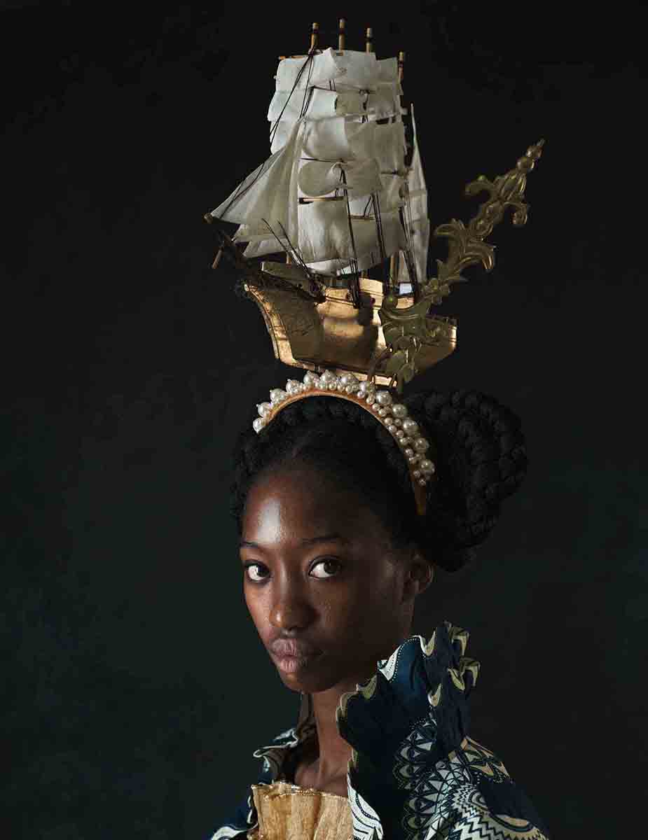A Black woman wears a headpiece shaped like a historic sail boat