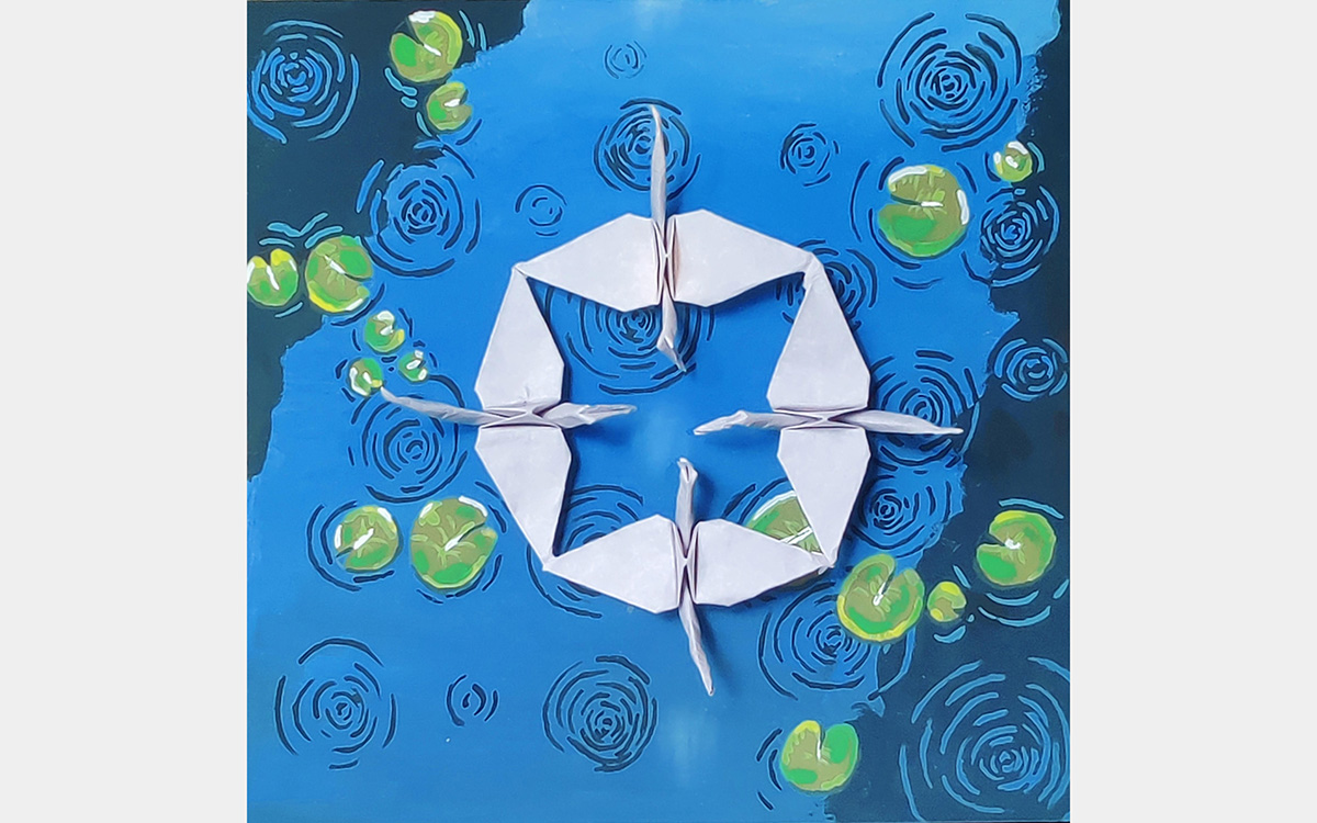Top view of four white origami cranes forming a circle on a blue background with green lily pads.