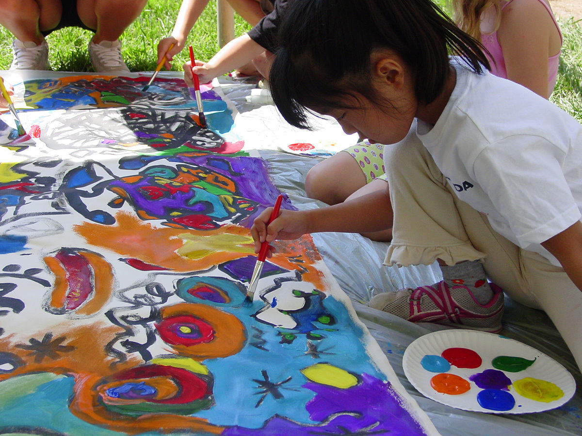 A young girl paints on a large group painting with several other people