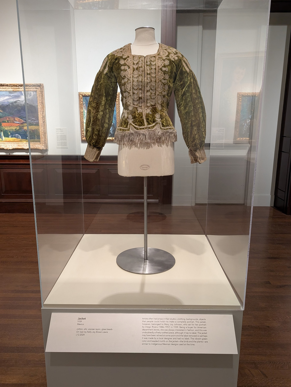 An ornate green jacket on a mannequin in a case