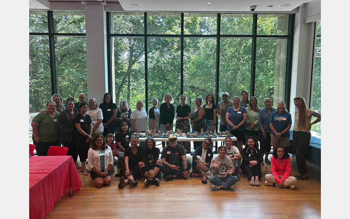 A group of 32 people pose in front of a glass curtain wall overlooking trees.