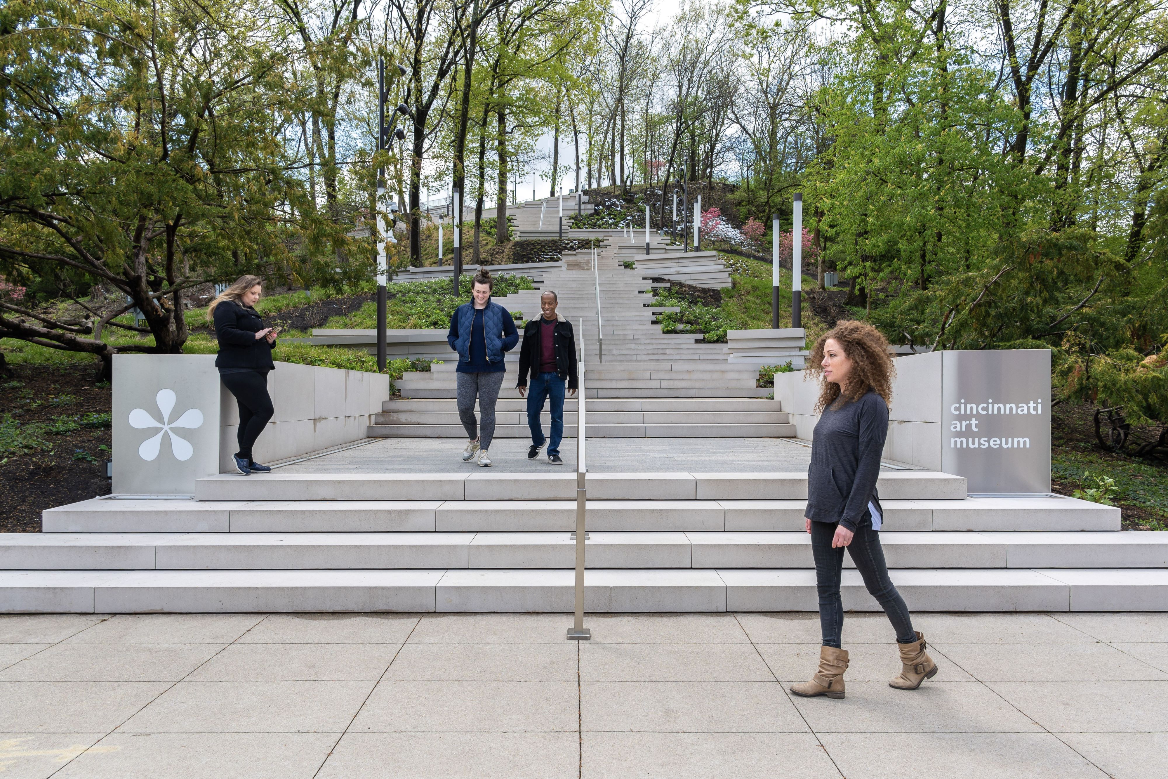 People walking at the bottom of an outdoor staircase that runs down a wooded hillside.
