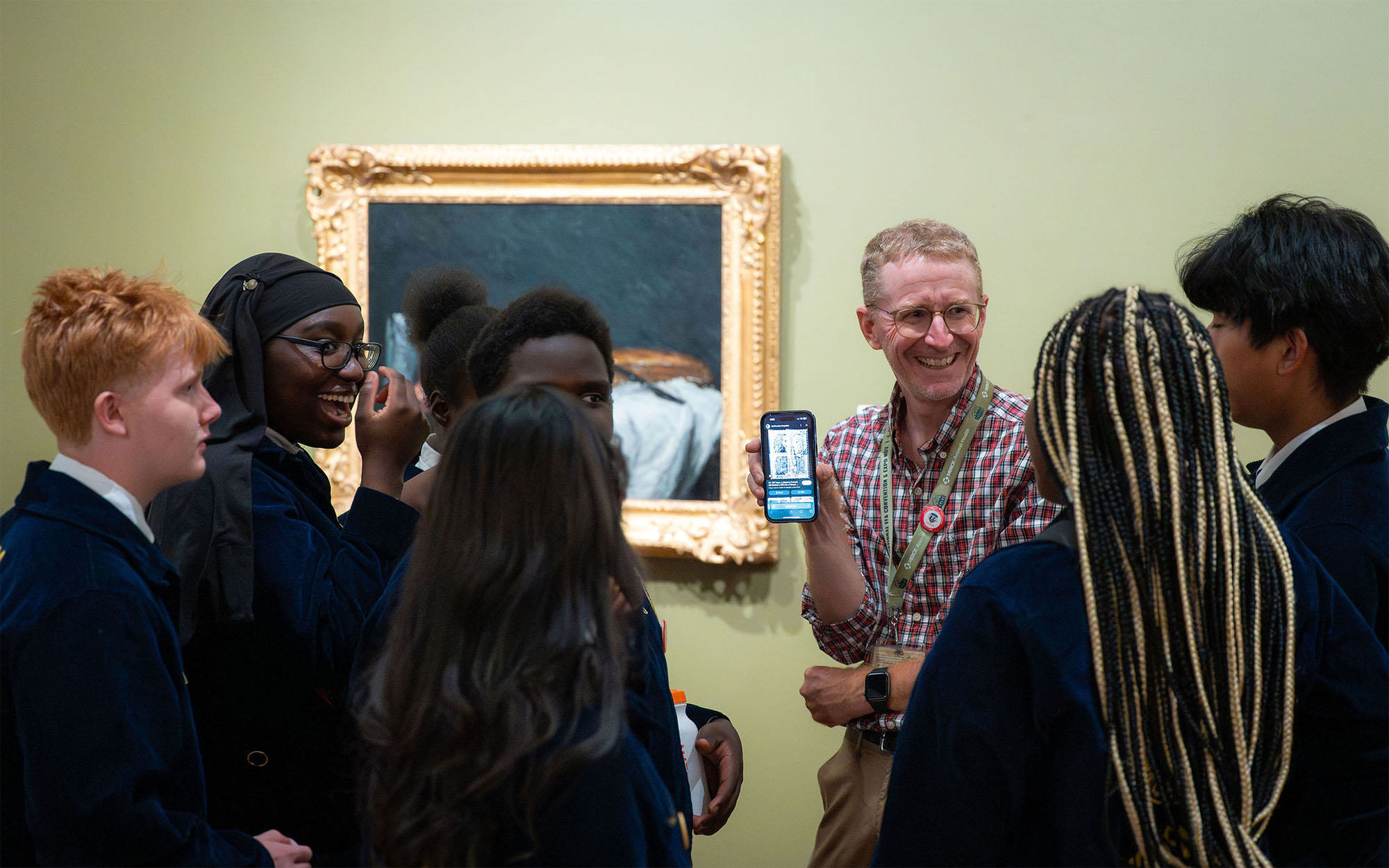 A tour guide smiles and shows their screen to a group of students