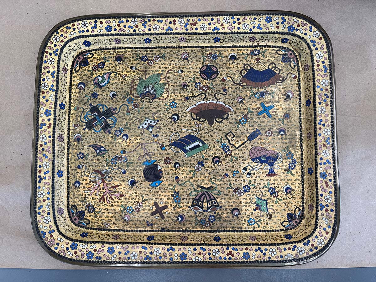 A decorated enamel tray. One corner is cleaner and lighter than the rest of the tray.