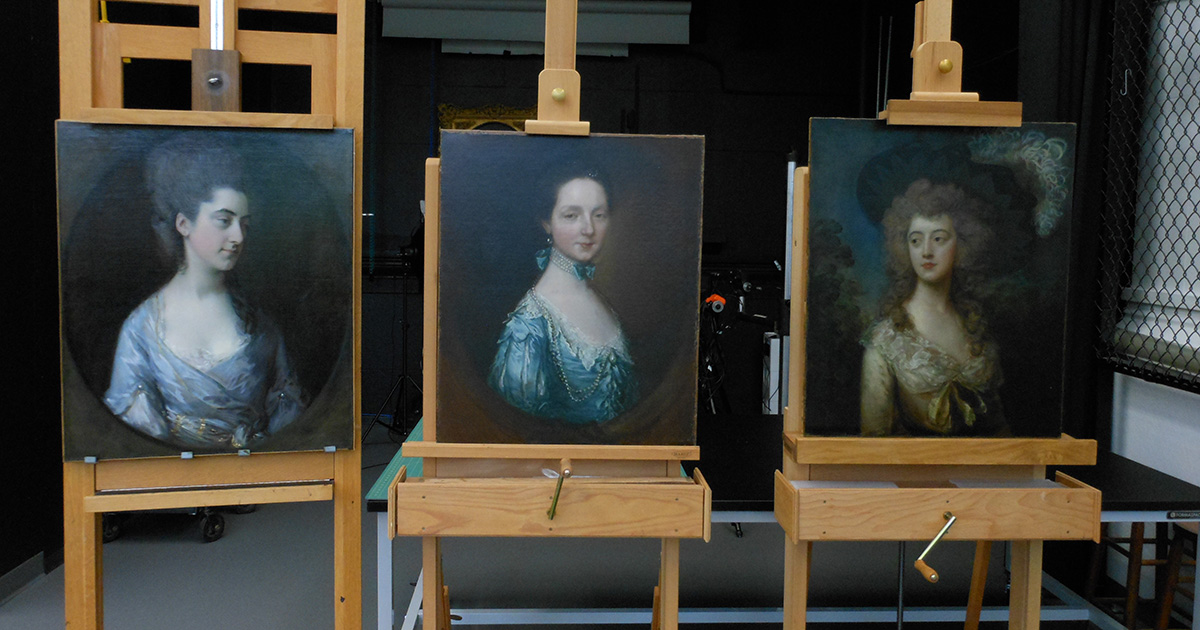 Three portraits of white women sit on wooden easels in the conservation lab.