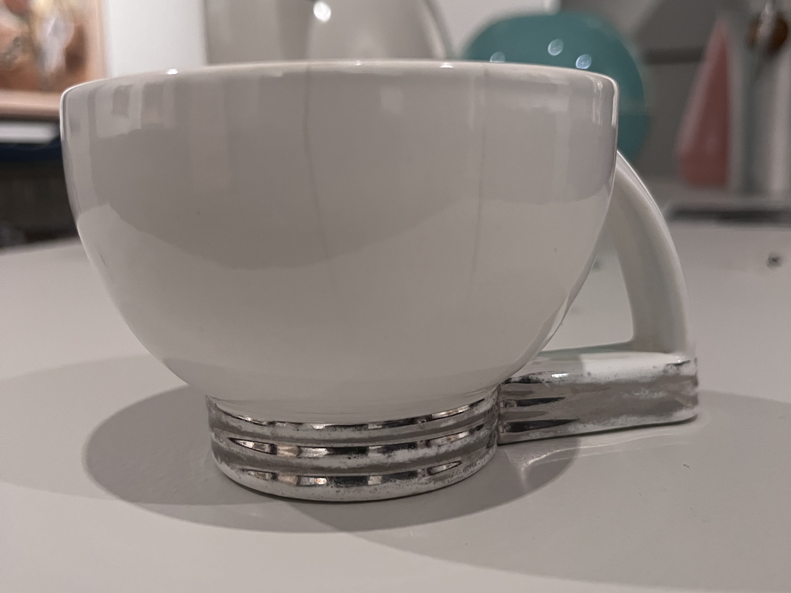 white ceramic teacup with chrome-colored ribbed base and angular handle