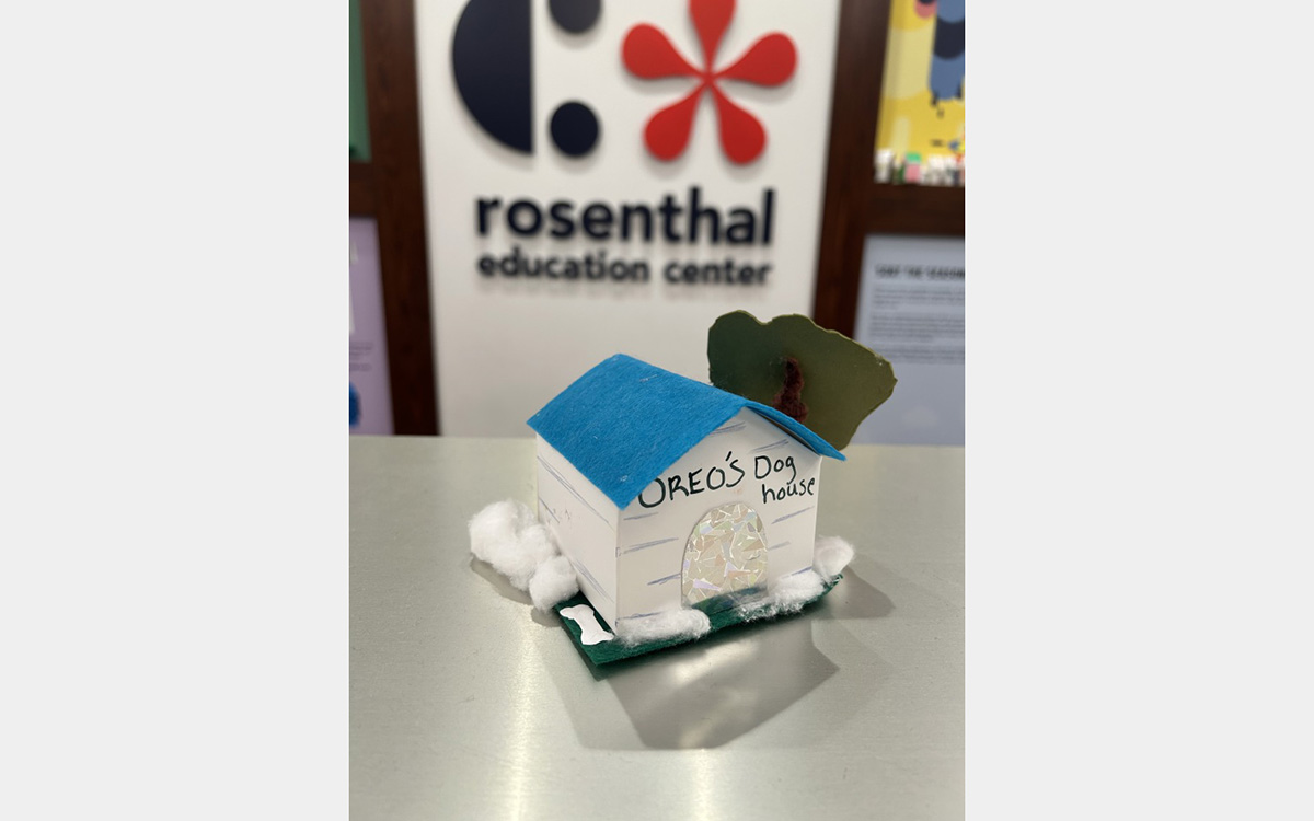 Small colorful model of a house on a tabletop with a "rosenthal education center" sign on wall in background.