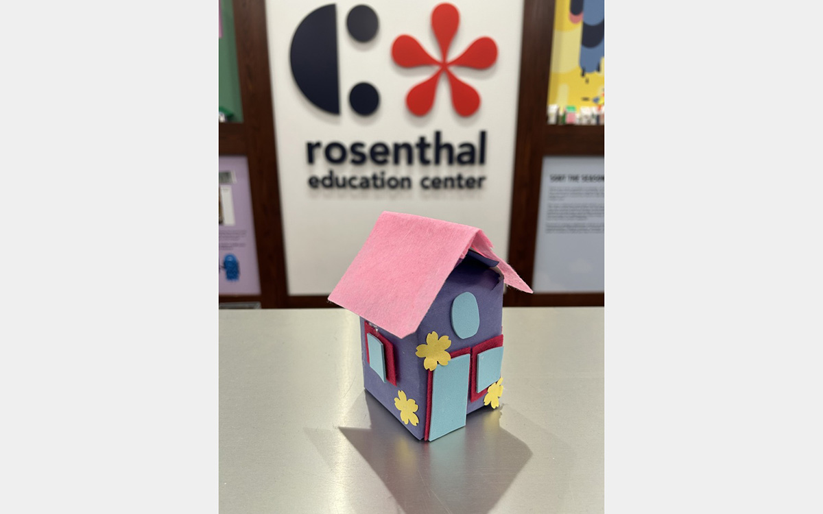 Small colorful model of a house on a tabletop with a "rosenthal education center" sign on wall in background.