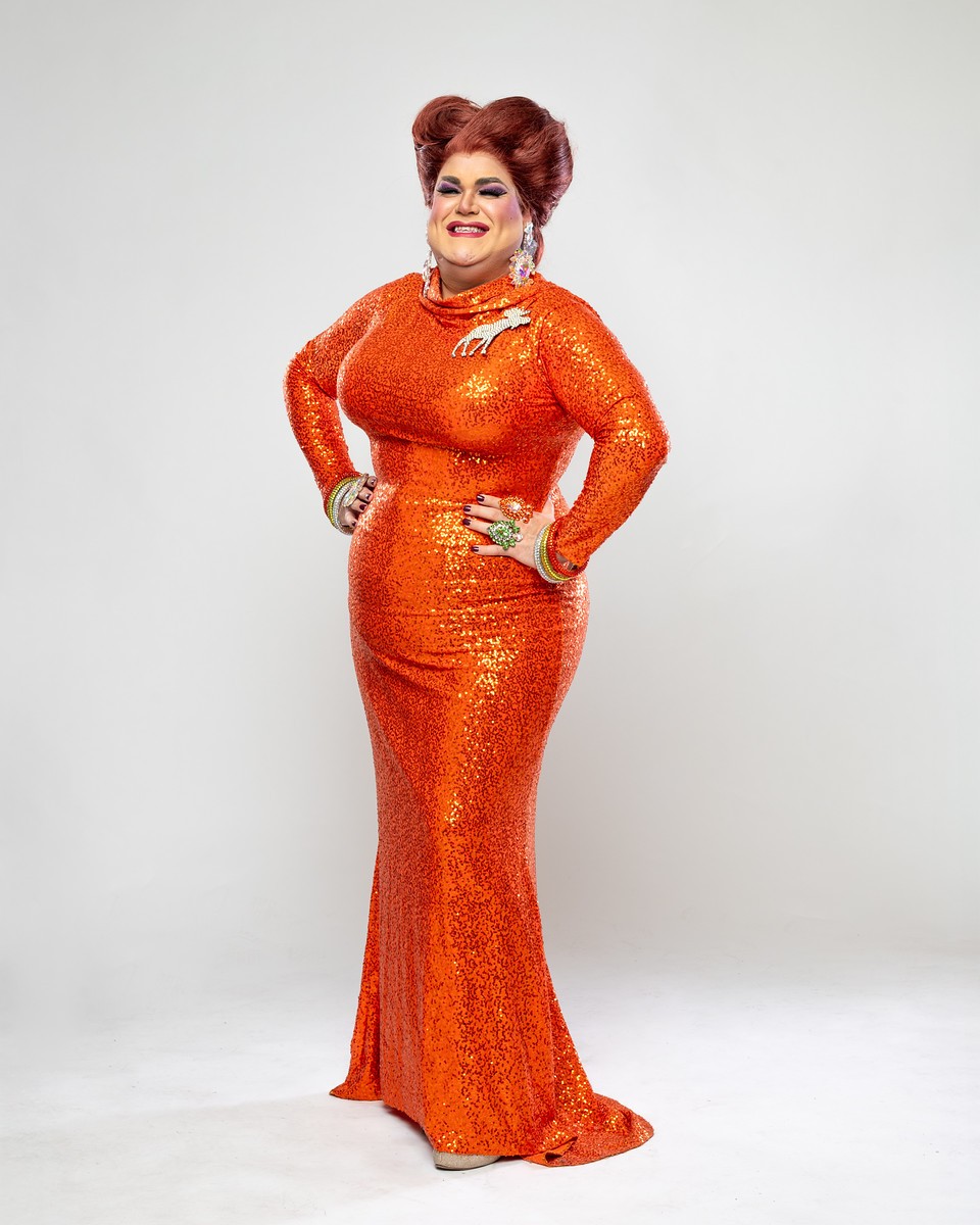 A smiling white person in a shiny orange gown