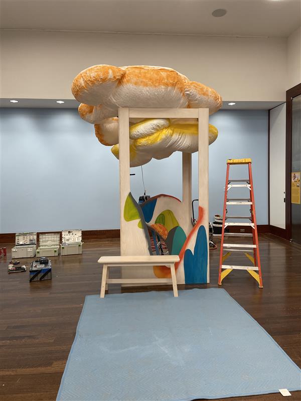Wood structure supports a cloud-like form next to a ladder.