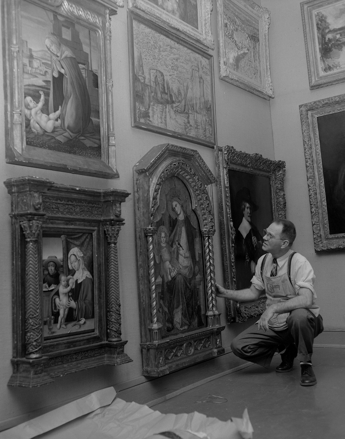 A black and white photo of a man crouching beside a framed painting in a gallery