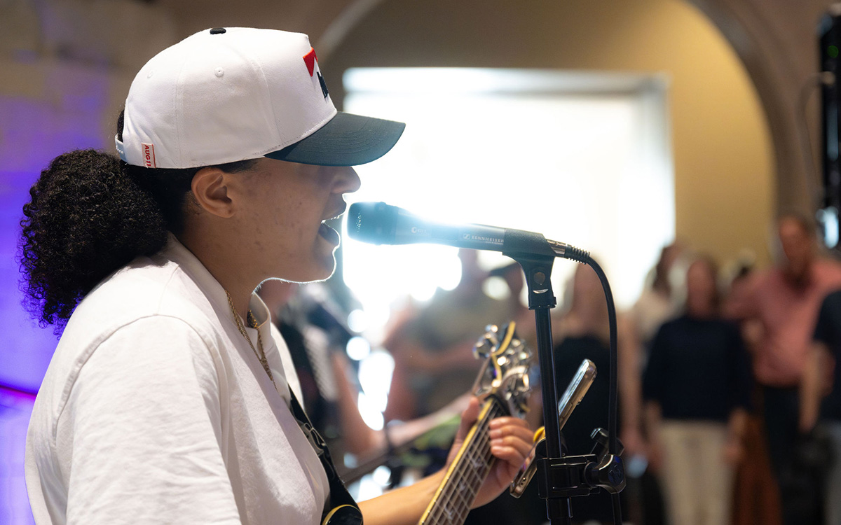 A Black performer sings into a mic while playing guitar
