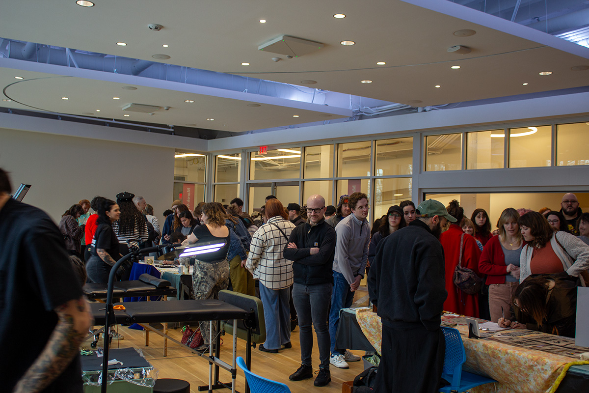 People crowd around tattoo artists displaying their designs