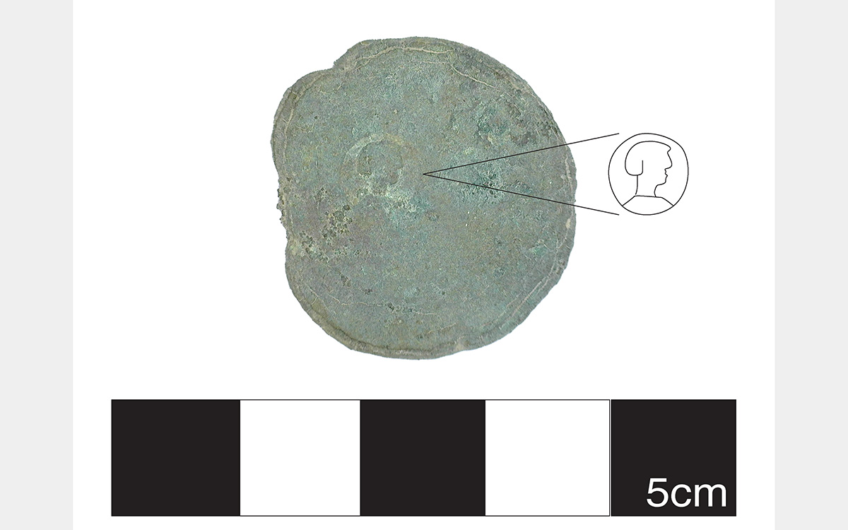 Greenish metal circle with a line drawing pointing to an incised design.