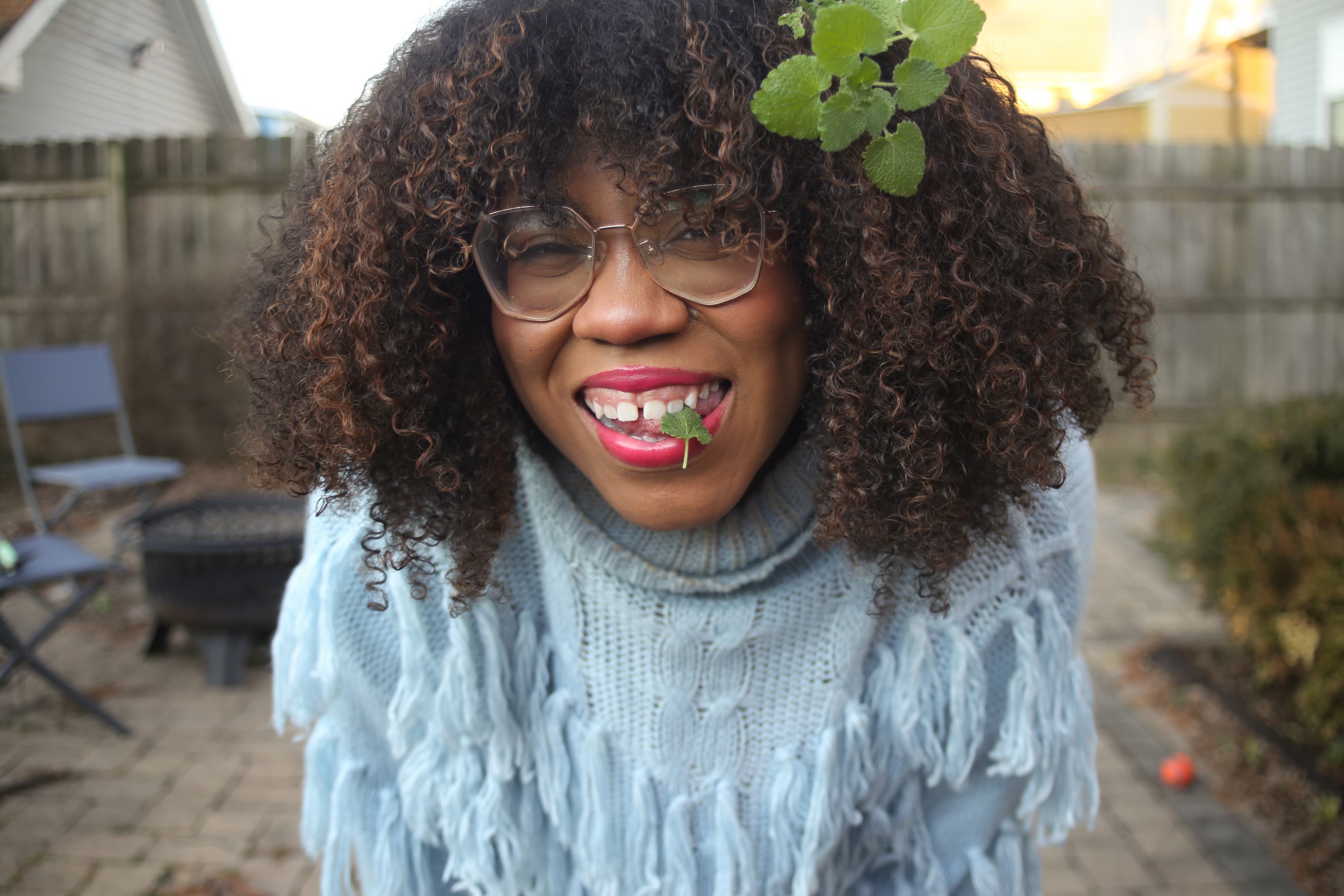 A Black woman smiles and chews on a leaf