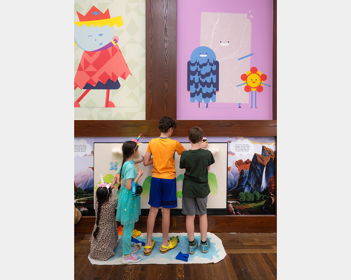 Two girls and two boys make a painting on a canvas attached to a wall.