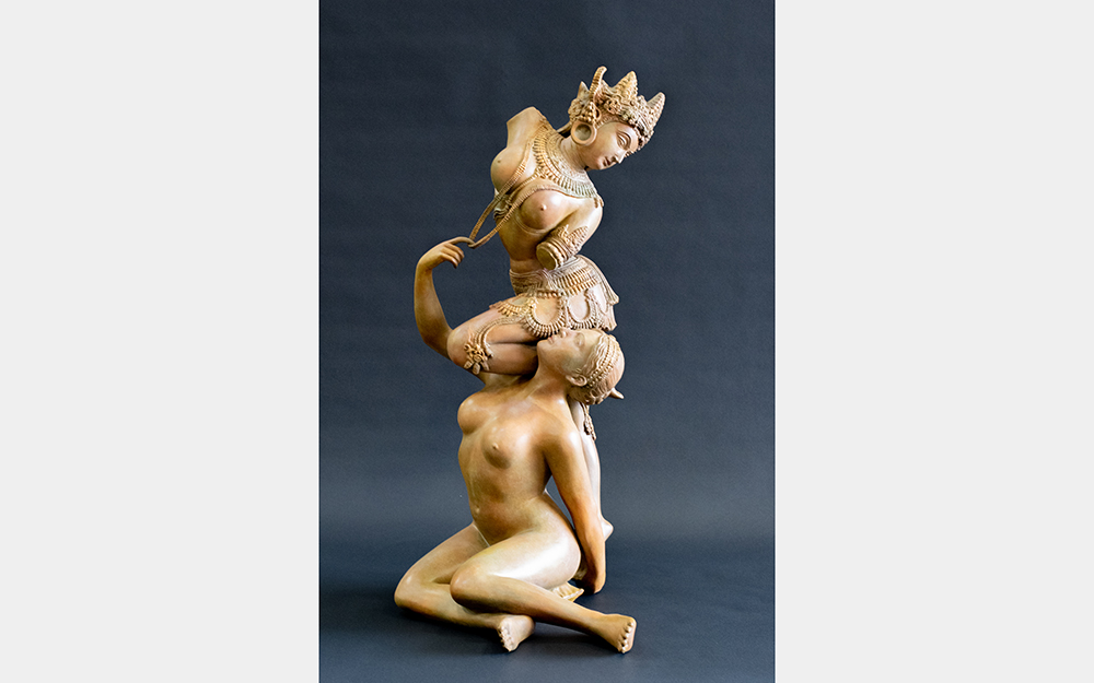 A sculpture of two nude women. One is sitting, and the other is kneeling on her shoulder