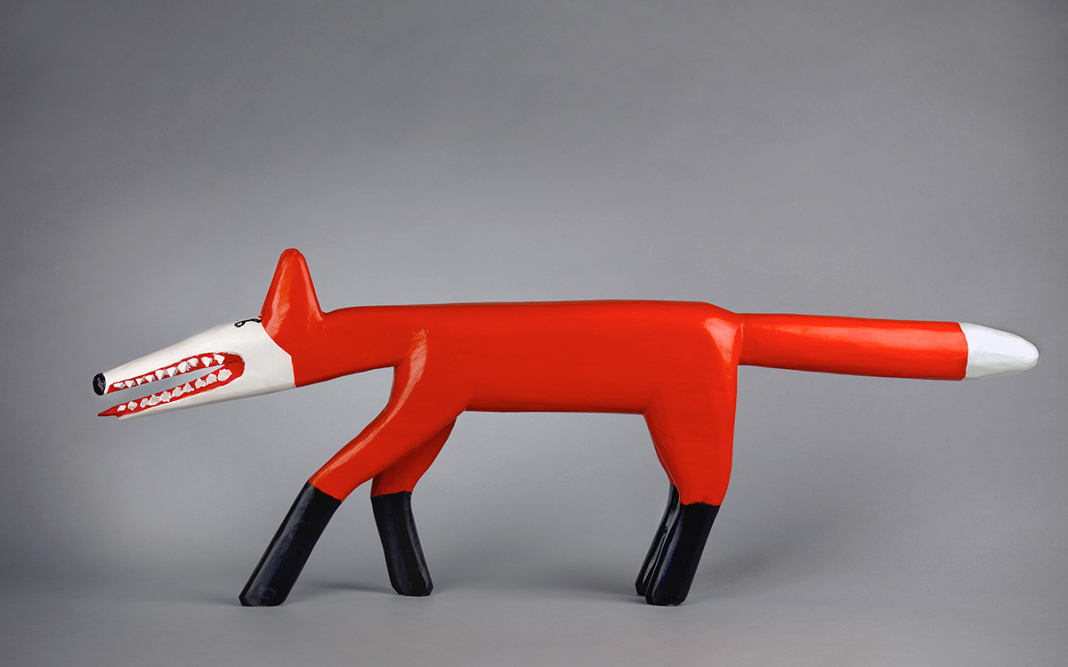 An abstracted wood carving of a fox painted in bright colors: red, white, and black.