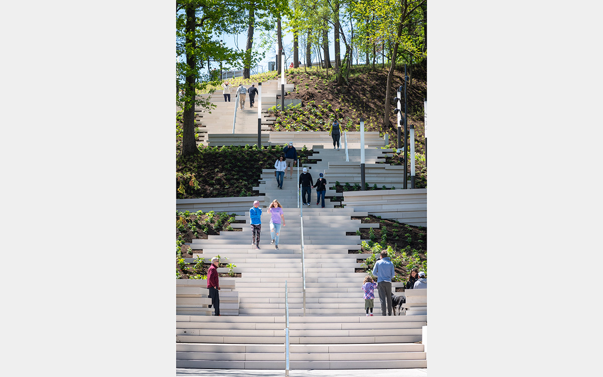 People walking up and down a wide staircase that zigzags up a tree covered hill.