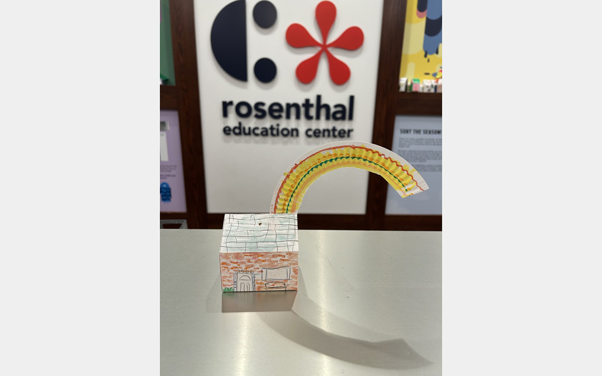 Small colorful model of a house on a tabletop with a "rosenthal education center" sign on wall in background.