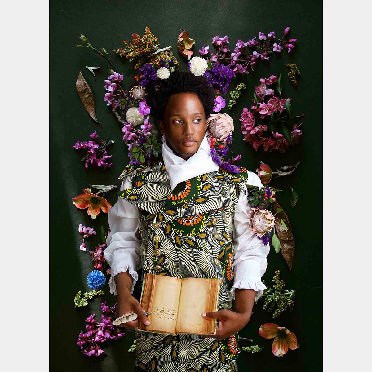 A Black man surrounded by flowers holds a book and a quill pen
