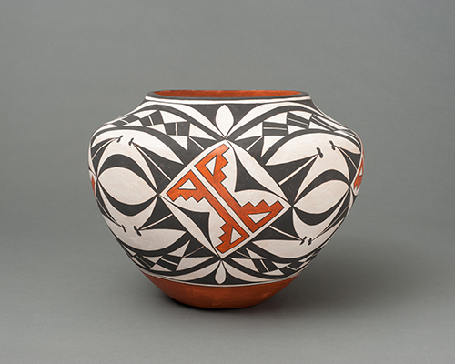 A painted ceramic vessel covered with sharp, black shapes and a geometric, orange design in the center.