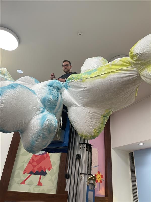 Installer on a lift preparing to mount cloud-like forms on the ceiling of a gallery.