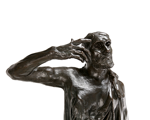 A rough, dark sculpture of a man wearing a robe with their hand reaching towards their face.
