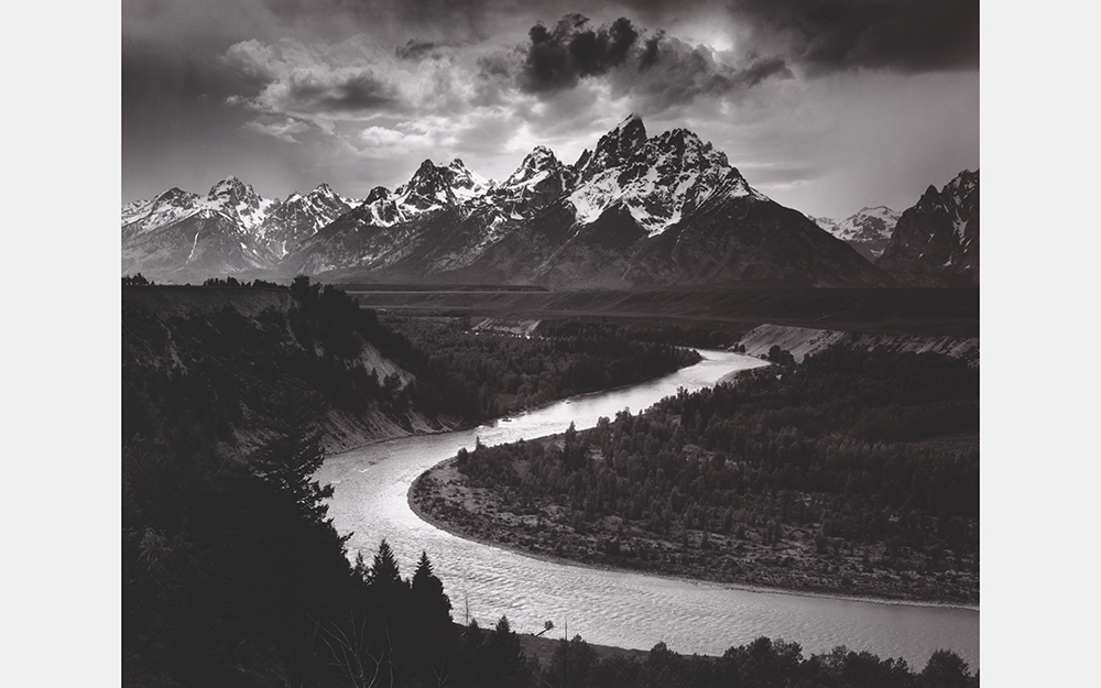A black and white photo of a twisting river in front of a jagged mountain range