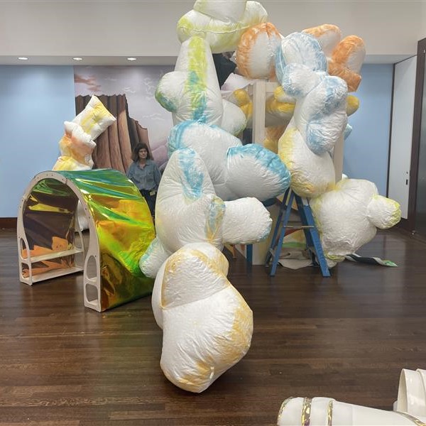 Artist Karen Saunders supervises the installation of cloud like forms in a gallery.