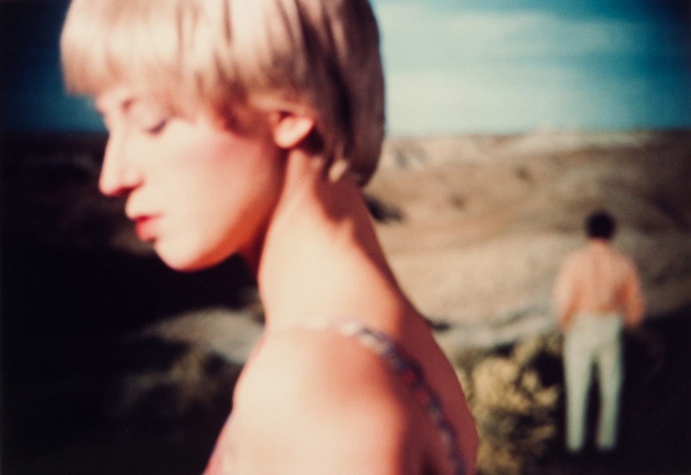 A color photo of a white woman with short blonde hair in front of a landscape