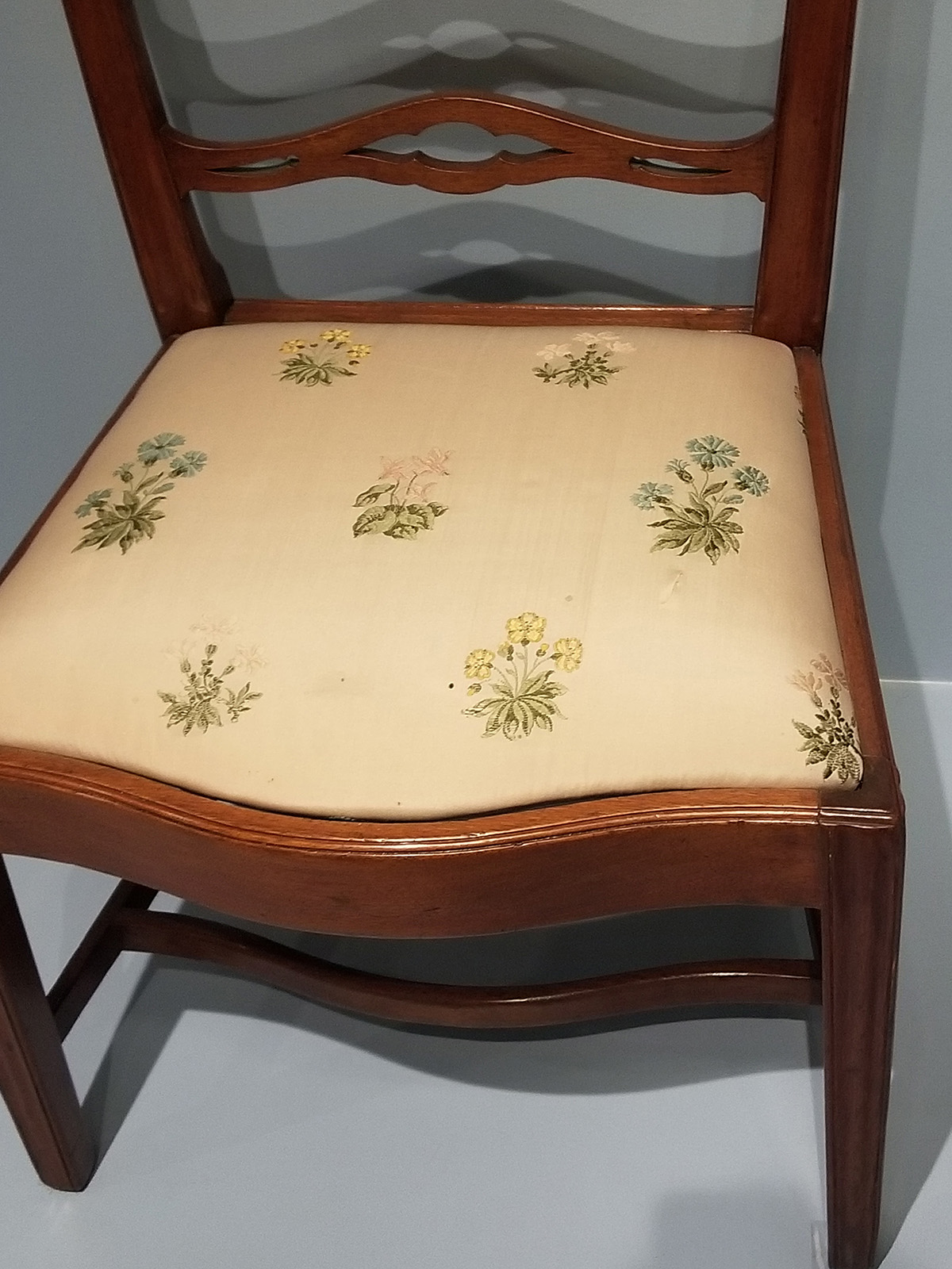 A chair with a faded fabric seat featuring embroidered flowers