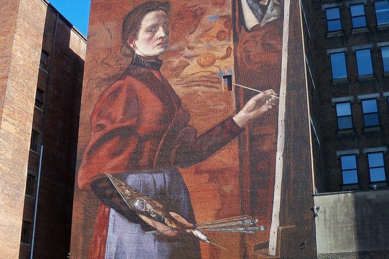 Outdoor mural depicting a woman painting with palette and canvass.