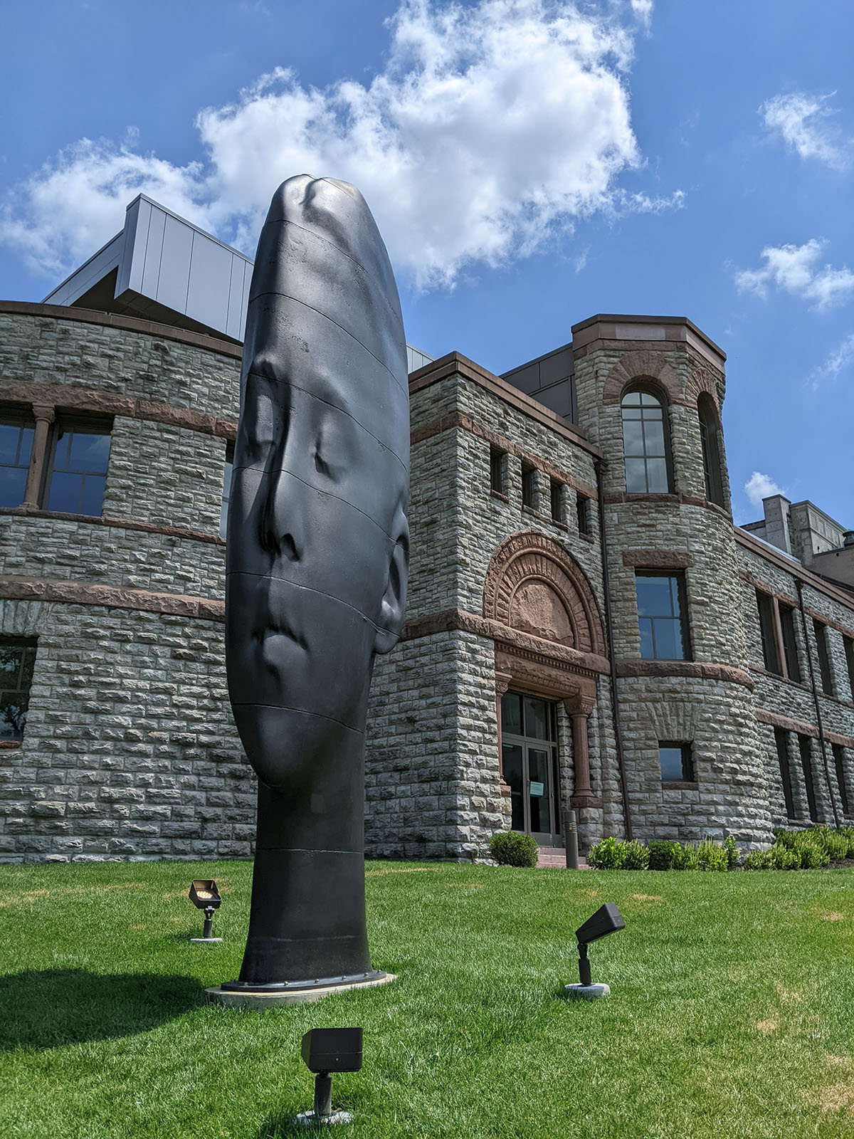 A monumental, thin black sculpture of a woman’s face in front of a stone facade