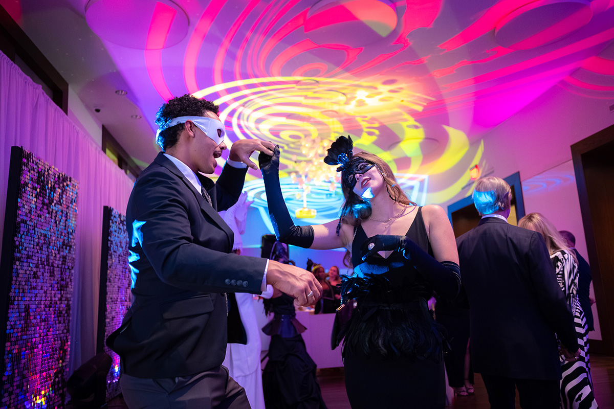 Two masked visitors dance in a colorfully lit room