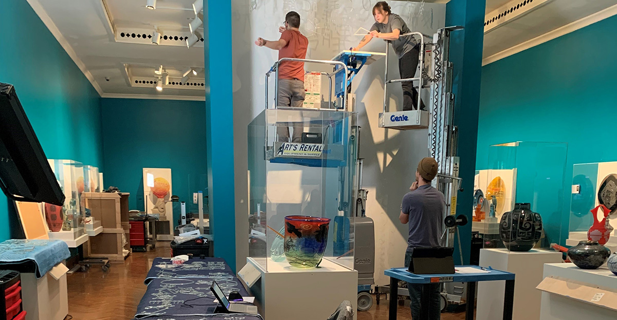 CAM staff installs hanging glass art in gallery
