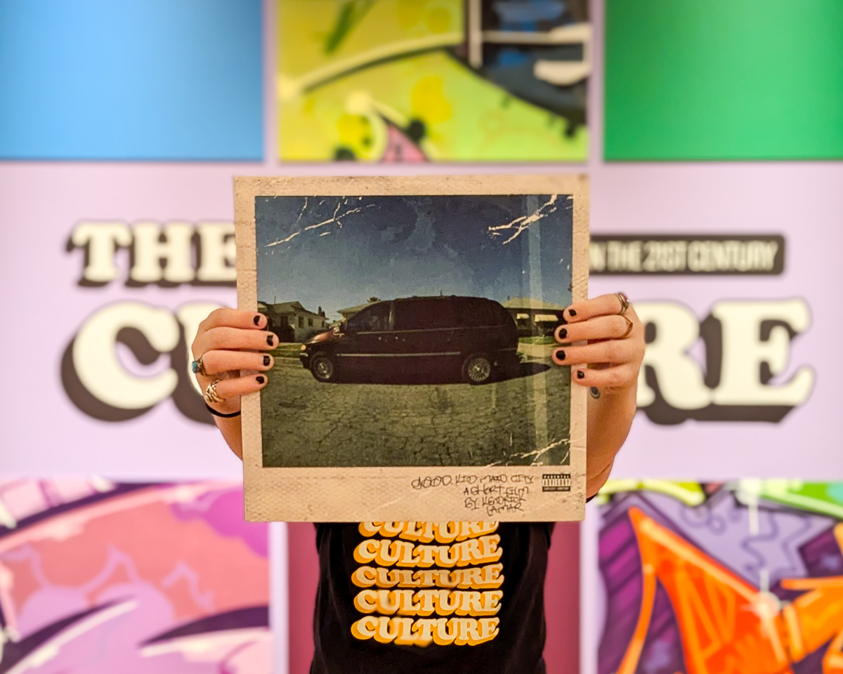 A pair of hands hold a vinyl copy of Good Kid M.A.A.D City in front of The Culture title wall