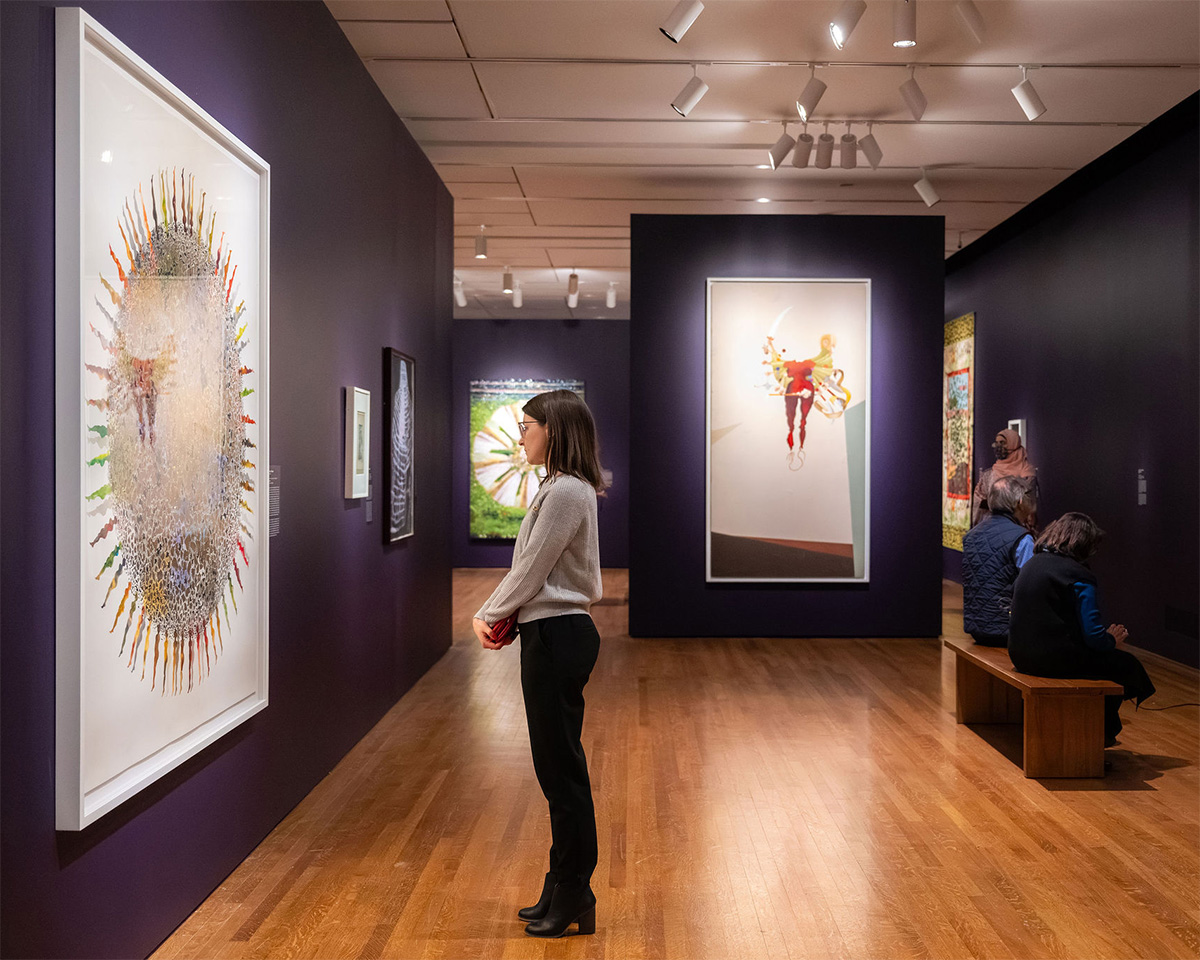 A white woman looks at a massive painting on a purple wall