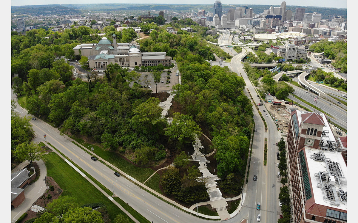 Aerial view of stone building on a green hill with a city skyline in the background.