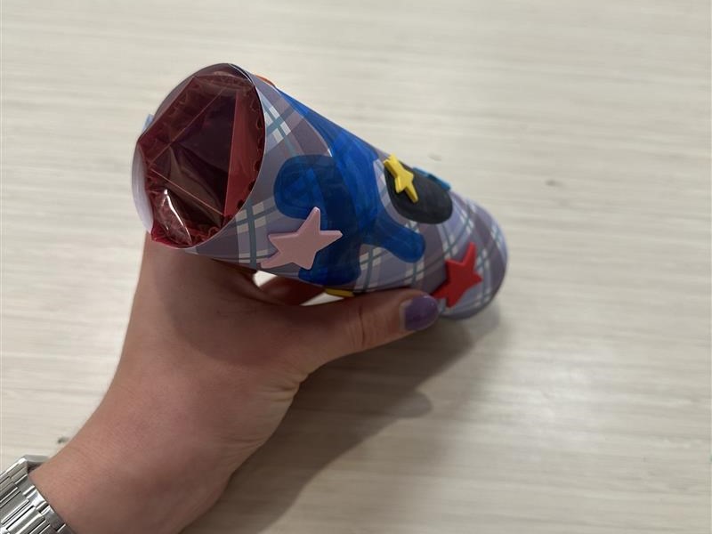 Hand holds a decorated paper tube encasing magenta-colored plastic.